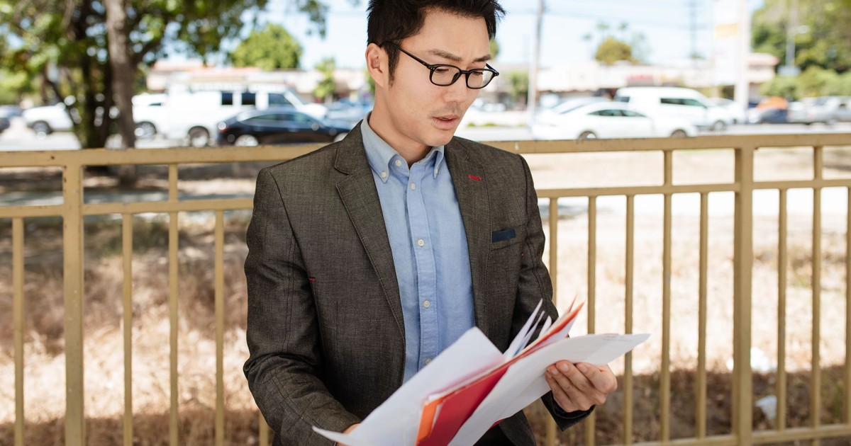 Asian businessman in a suit checking documents outdoors on a sunny day.