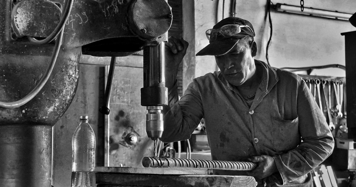 Monochrome image of an industrial worker using a drill press in a workshop setting.