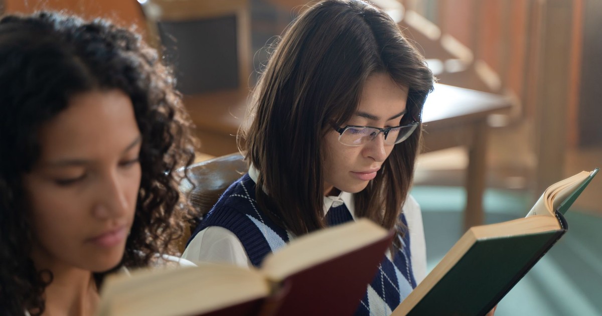 Two female students reading books in an educational setting. Perfect for school and study themes.
