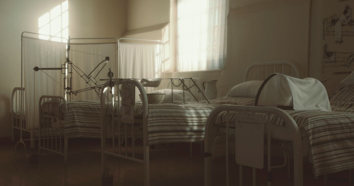 Dimly lit vintage hospital room featuring empty beds and medical equipment, creating a nostalgic atmosphere.