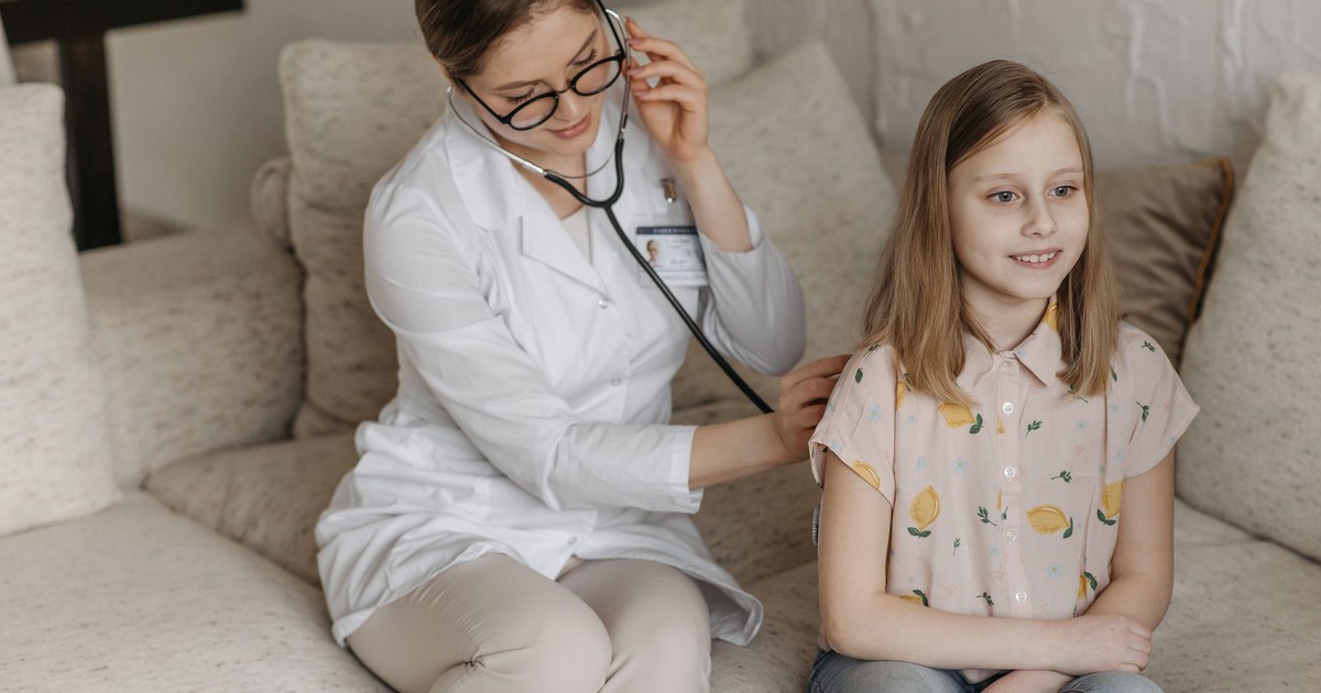 Doctor using a stethoscope for a child's check-up on a sofa during a home visit.