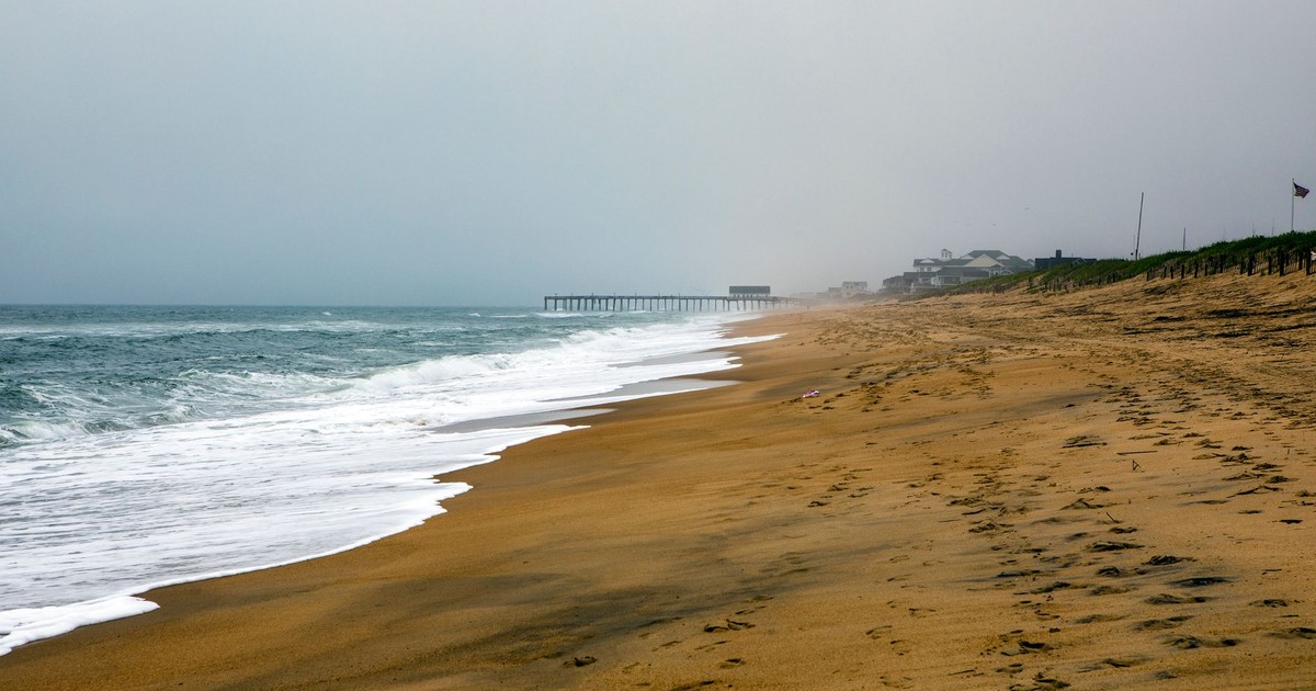 Serene view of Nags Head beach with gentle waves and a distant pier, ideal for relaxation.