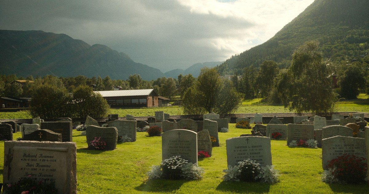 Scenic cemetery surrounded by lush mountains and cloudy sky, capturing tranquility and nature.