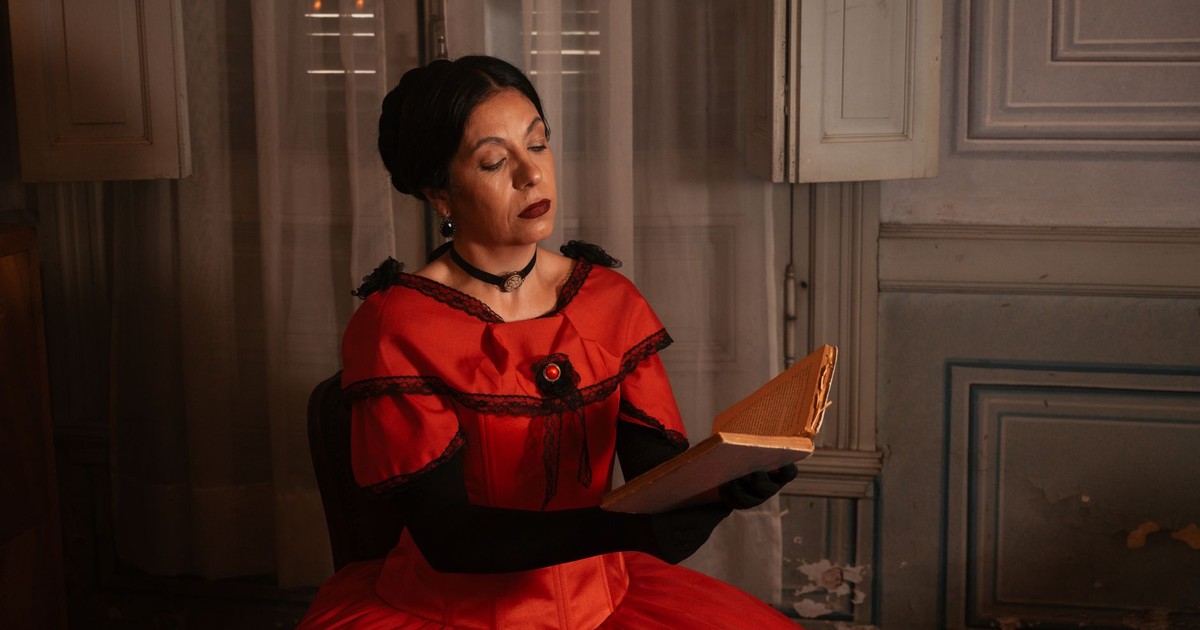 A woman in a red Victorian-era dress is reading a book indoors, evoking a historical and elegant ambiance.
