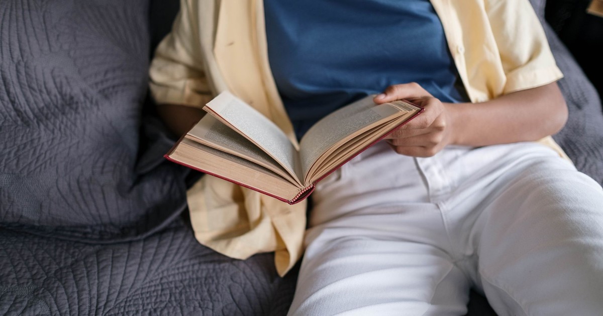An adult casually reading a book while reclining on a comfortable sofa indoors.
