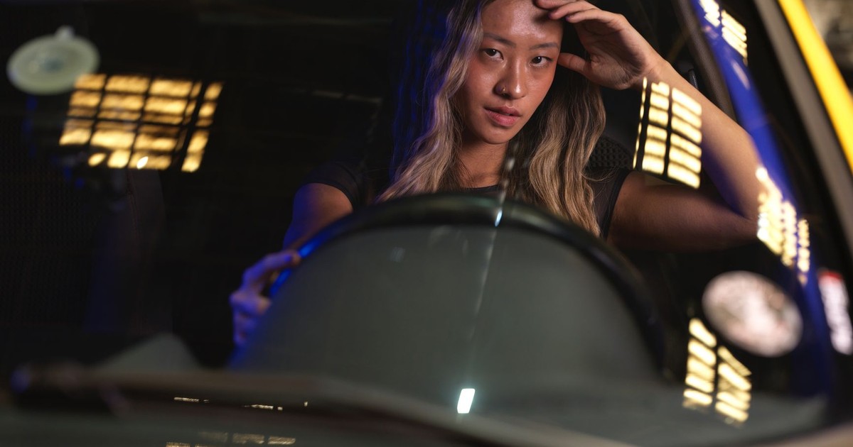 A young woman sits in a car at night, looking focused as she drives under city lights.