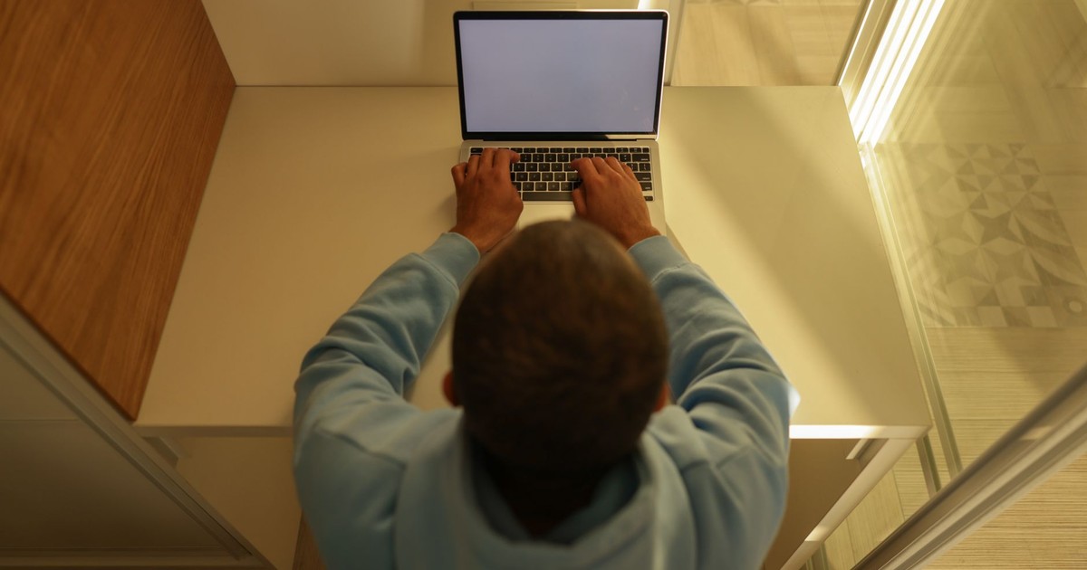 Overhead view of a man typing on a laptop with a blank screen, wearing a hoodie, sitting at a desk.