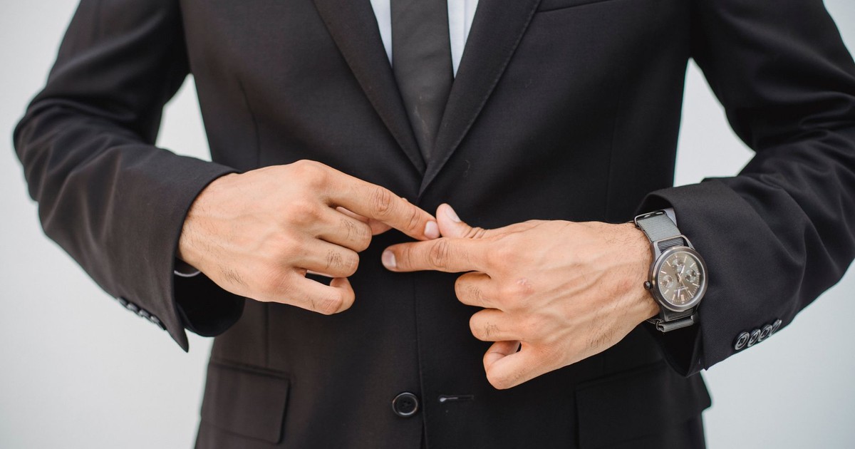 Close-up of a man's hands adjusting a black suit jacket, showcasing confidence and style.