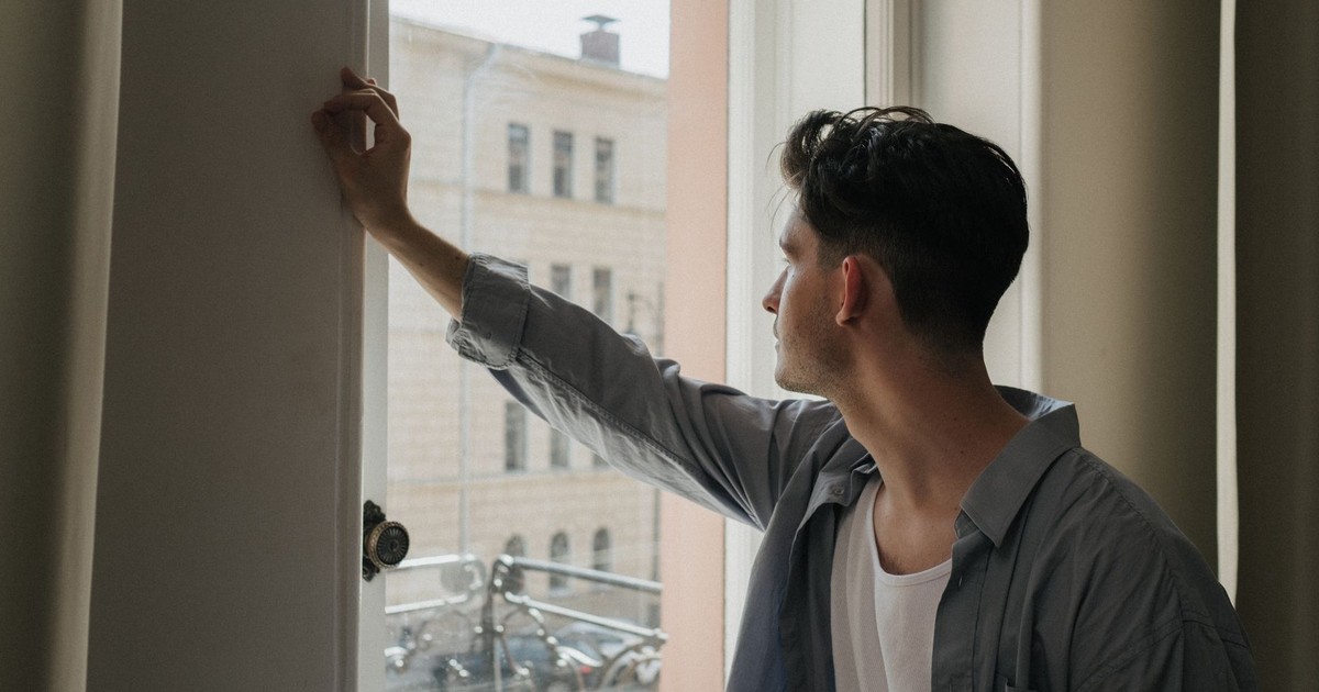 A man gazes thoughtfully out a window in a well-lit room, capturing a moment of introspection.