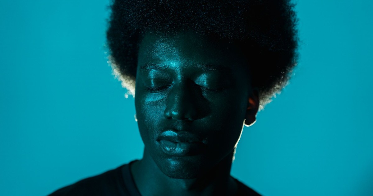Close-up of an African American man with afro hair against a blue background.
