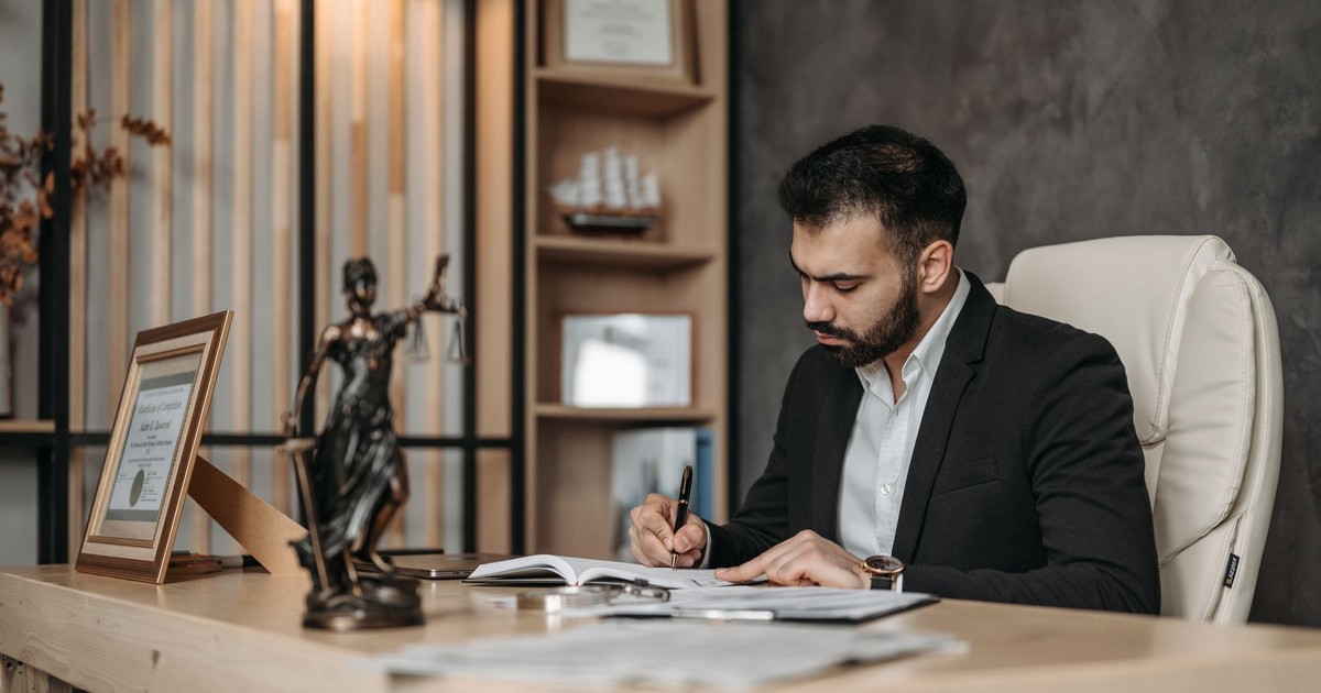 A focused lawyer in an office setting writing and reviewing legal documents, symbolizing expertise and professionalism.