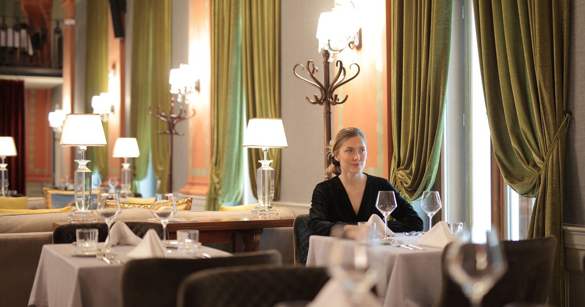 A woman seated alone at a beautifully set table in an upscale restaurant with elegant decor.