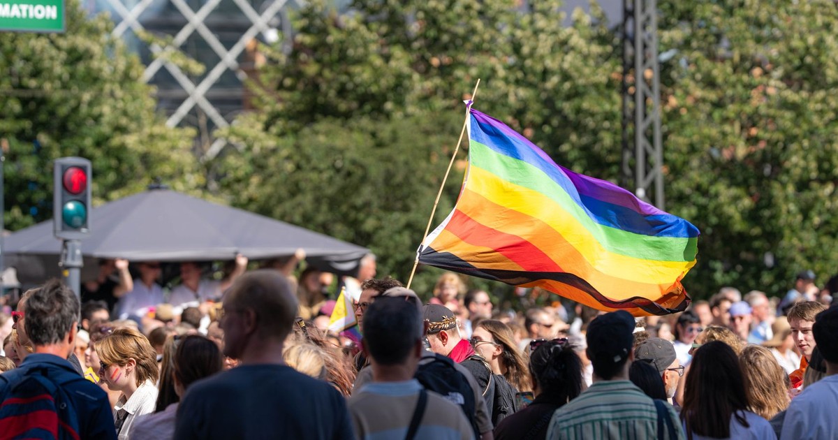 Vibrant pride parade scene with a waving rainbow flag amidst a diverse crowd outdoors.