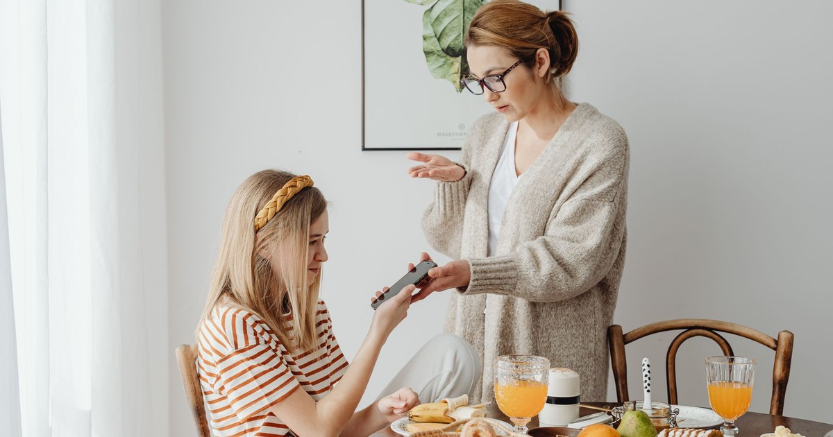 A mother and daughter in a discussion over phone use during breakfast at home.