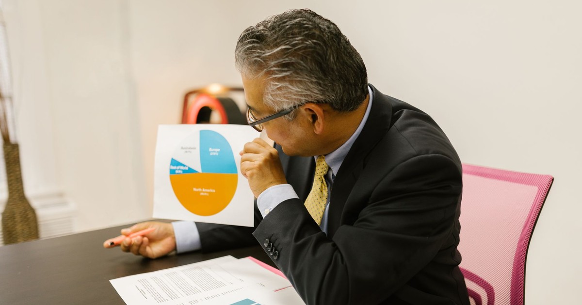 A businessman in a suit reviews pie chart documents at his office desk.