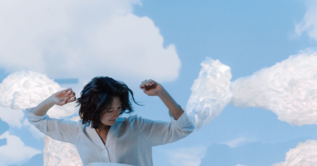 Asian woman with short hair in white shirt surrounded by clouds, evoking peaceful dreaming.