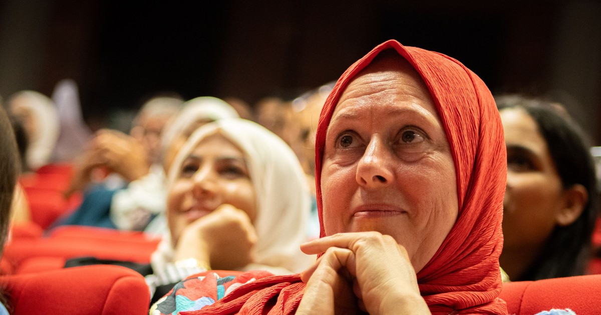 Diverse audience members attentively watching a speaker at a cultural event indoors.