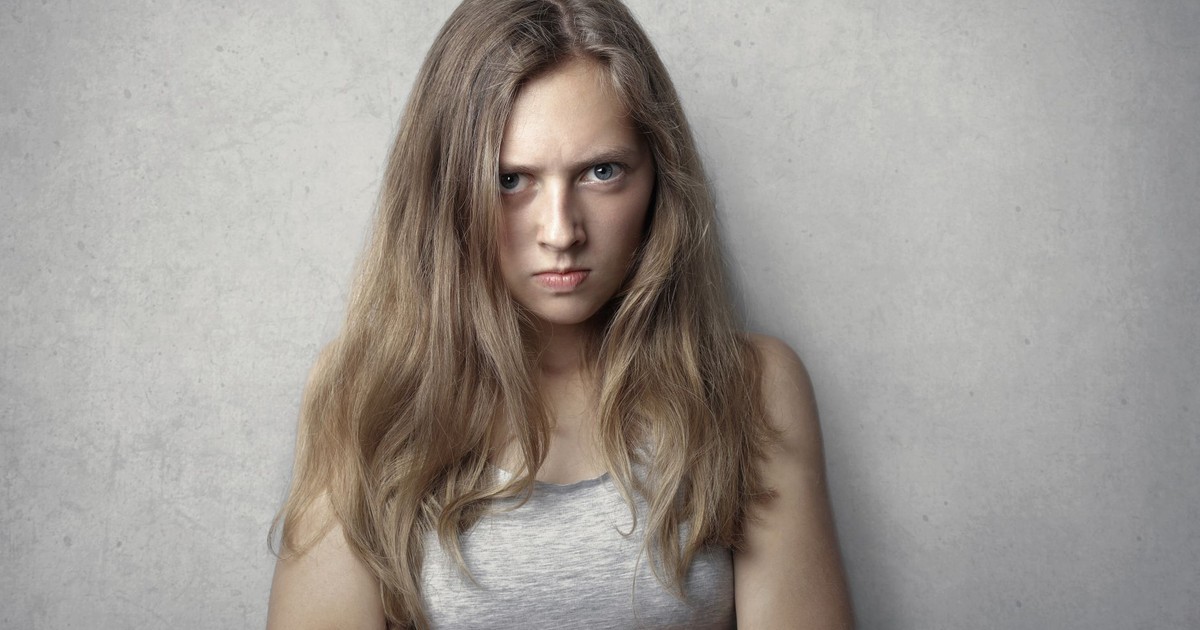 Portrait of a fierce woman with crossed arms and intense expression on a gray background.