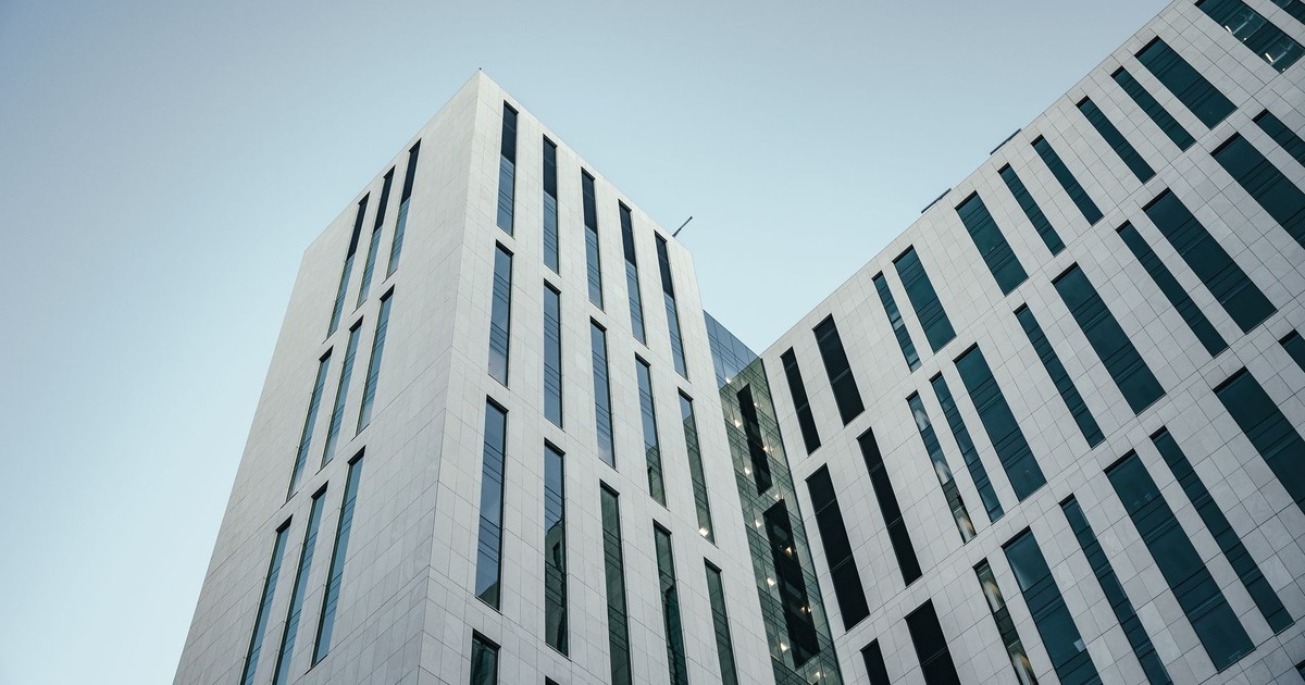 From below of contemporary multistory building with futuristic design and windows with unusual shapes located against cloudless blue sky on street of city