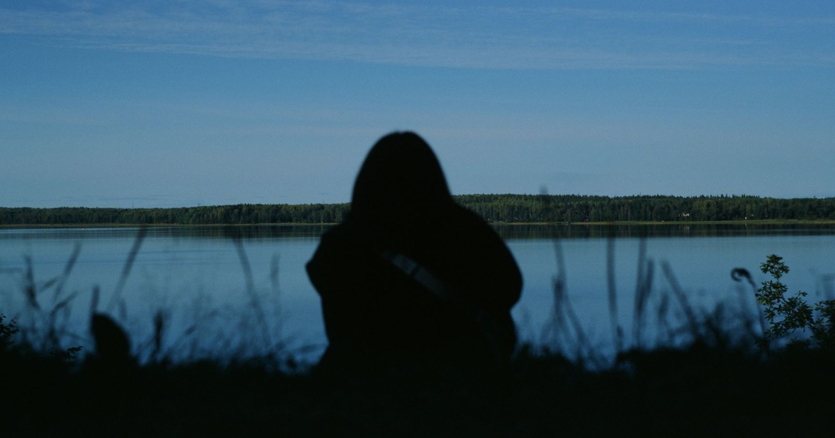 Silhouette of a person by a calm lake during a peaceful day.