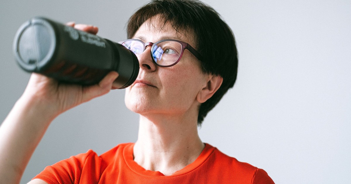 Caucasian senior woman in glasses drinking from a bottle, promoting active lifestyle.