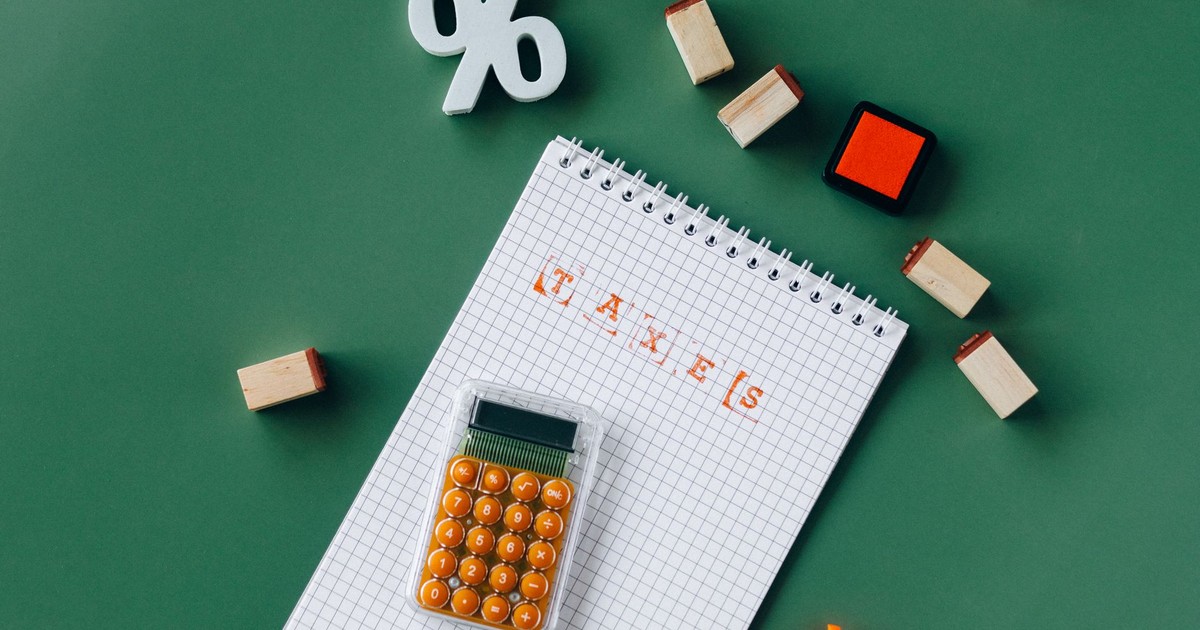 Flat lay of tax essentials with calculator, notebook, and stamps on a green background.