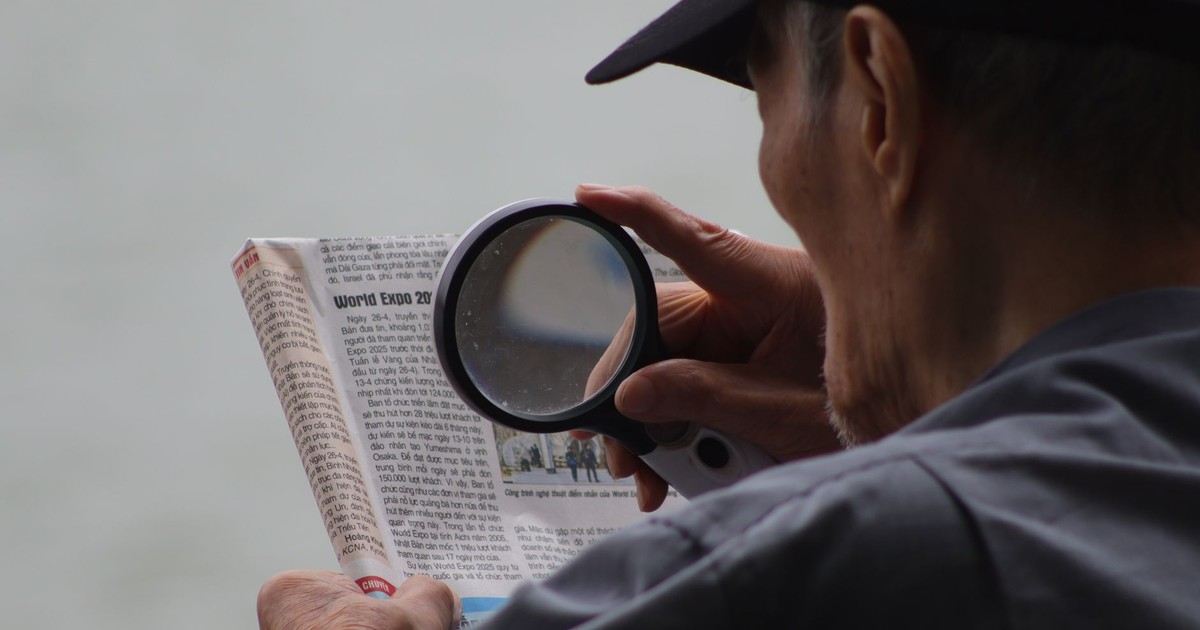 Elderly man using a magnifying glass to enhance text in a newspaper.
