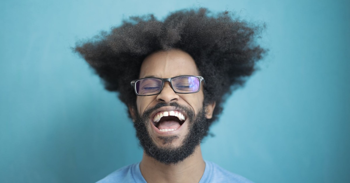 Happy man with afro hair and glasses laughing joyfully against a blue background.