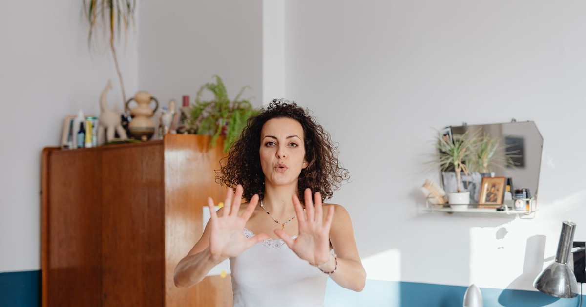 A woman with curly hair practices mindfulness exercises indoors, surrounded by plants.
