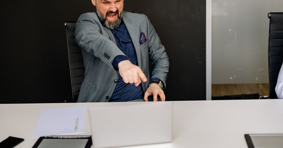 A businessman expressing frustration while pointing at a laptop in a modern office setting.