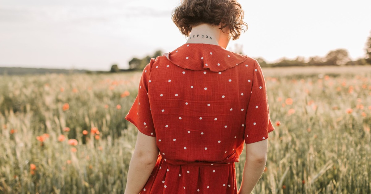 Back view of a woman in a red polka dot dress standing in a field with wildflowers at sunset.