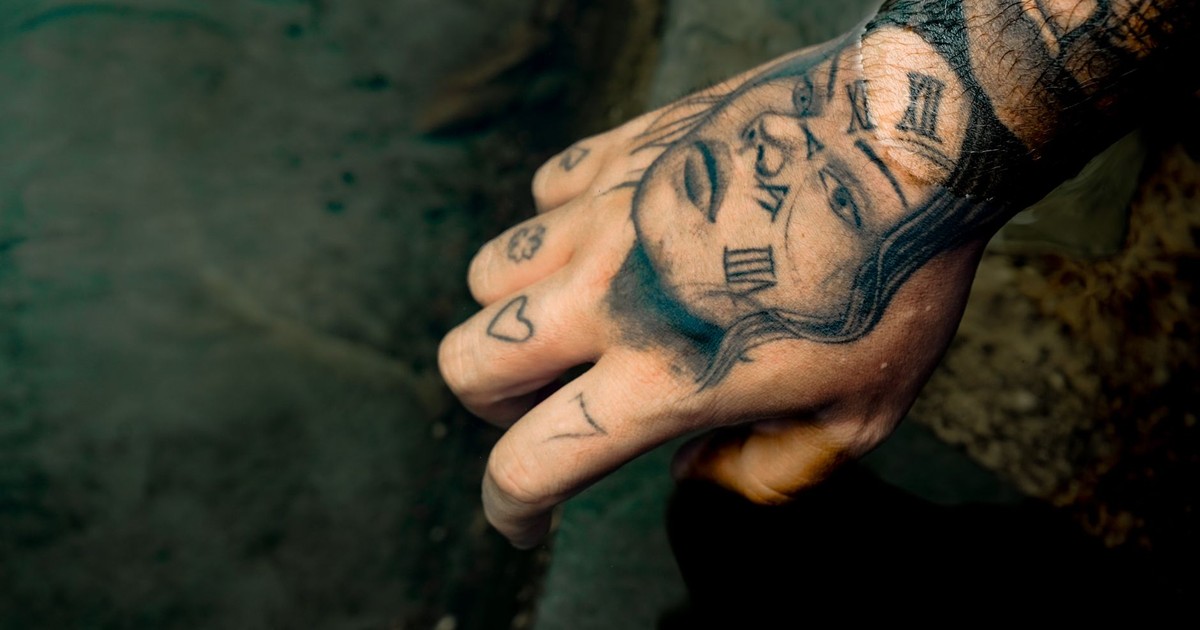 A detailed shot of a hand with expressive tattoos including Roman numerals and faces.