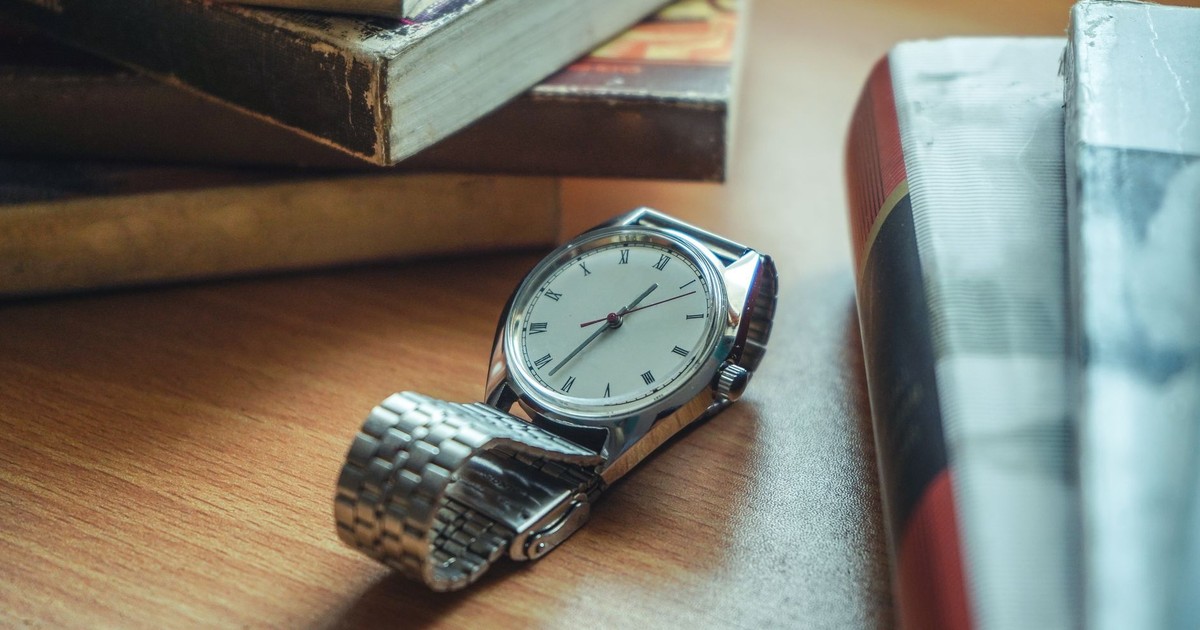 Close-up of a classic analog wristwatch placed on a wooden desk near stacked books.