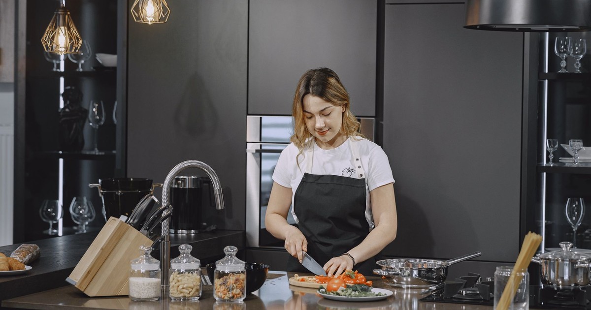 A woman slices vegetables on a kitchen counter under elegant lighting.