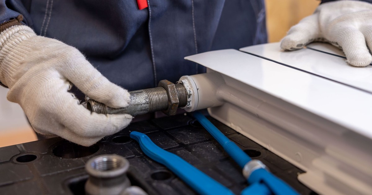 Close-up of a plumber installing a radiator pipe using specialized tools.