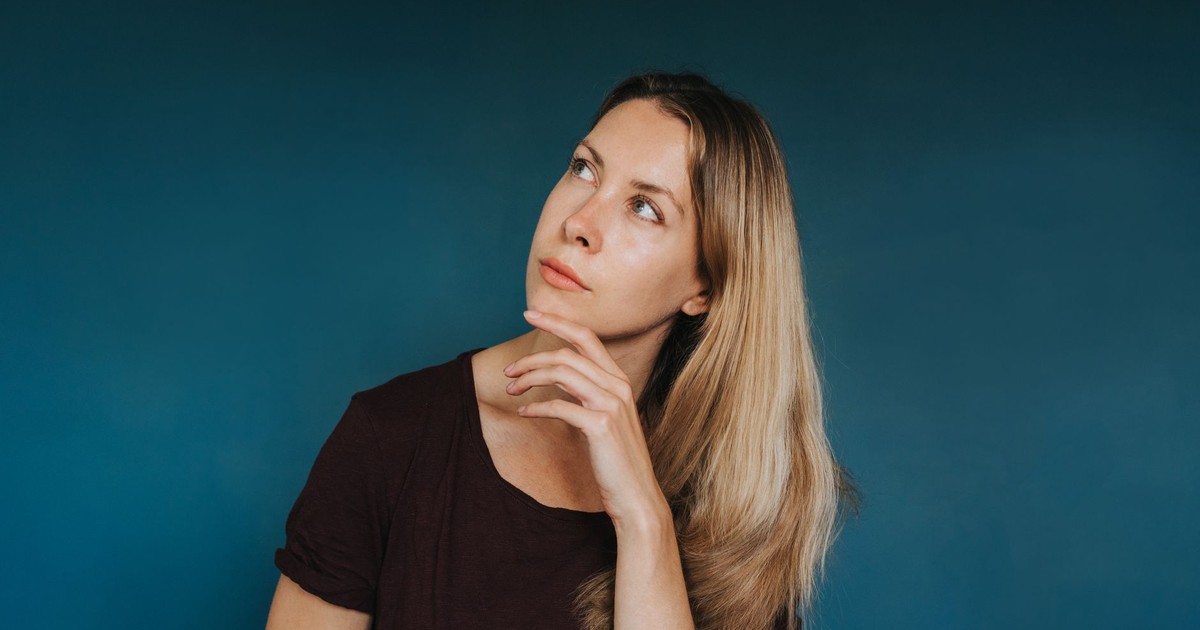 Young thoughtful female in casual clothes touching chin while standing in studio and looking up