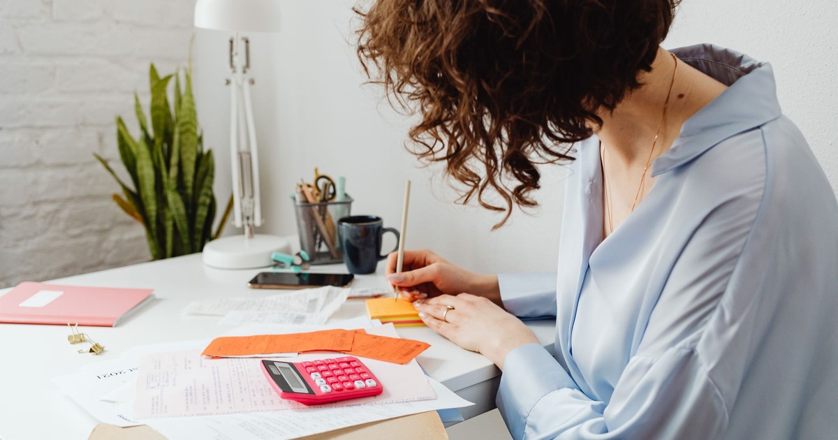 Woman writing with calculator on desk, managing finances indoors.