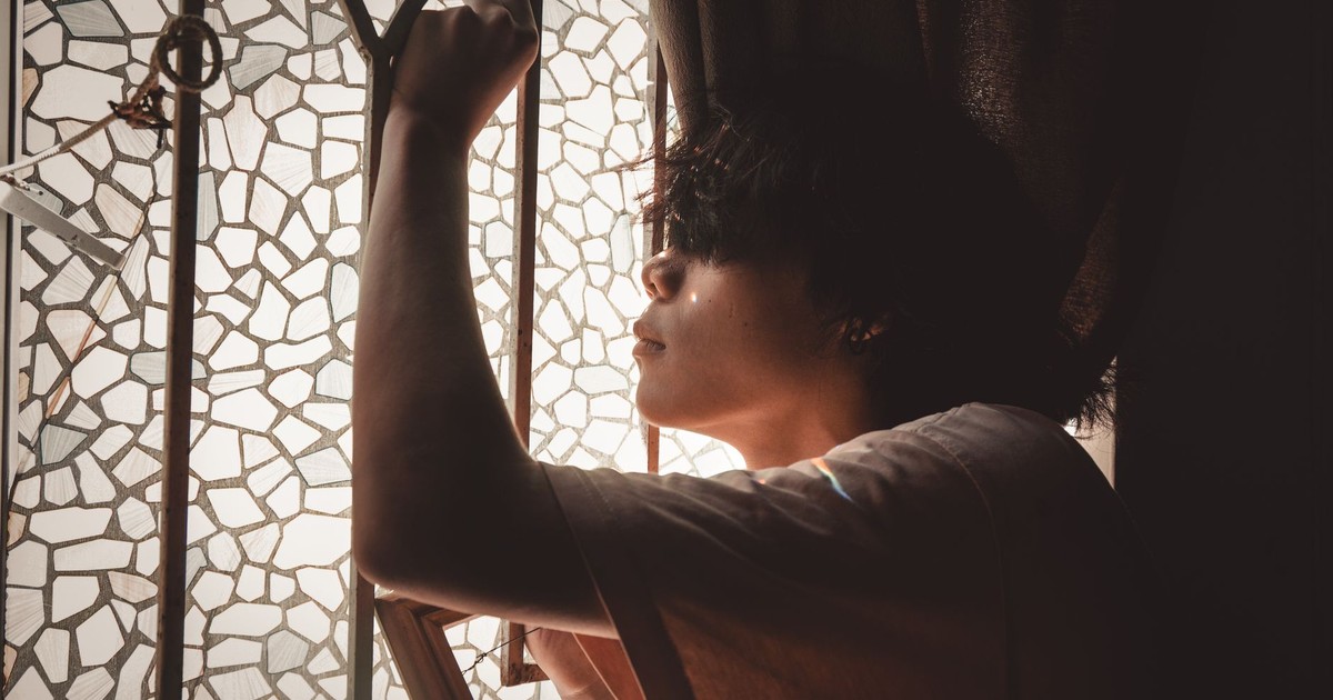 Side view of a young man posing thoughtfully by a mosaic glass window with soft light.