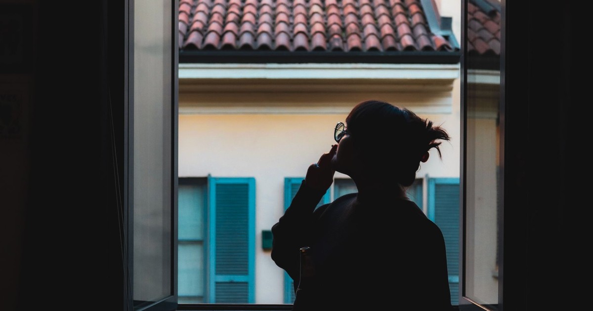 Silhouette of a woman in a serene moment by the window, viewing the tiled roof outside.