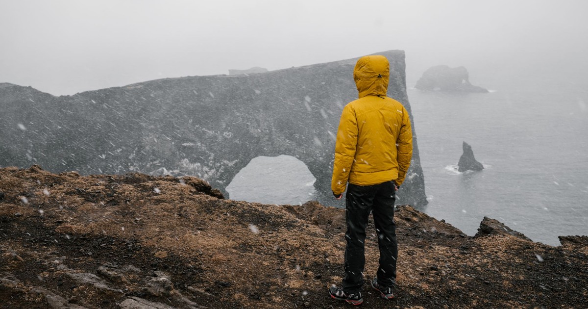 Yellow-jacketed person on a snow-covered cliff by the sea, facing a dramatic seascape in winter.