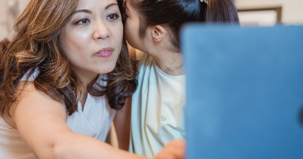 A mother and daughter share a close moment while whispering indoors.