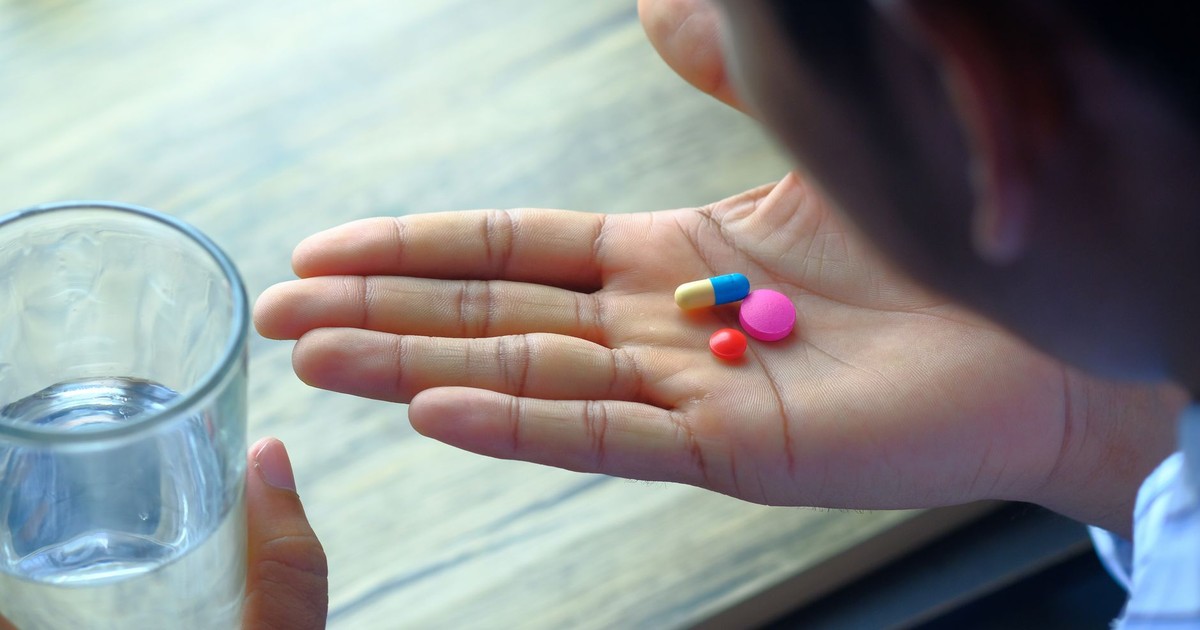 A hand holding a variety of pills alongside a glass of water, emphasizing health and medication.