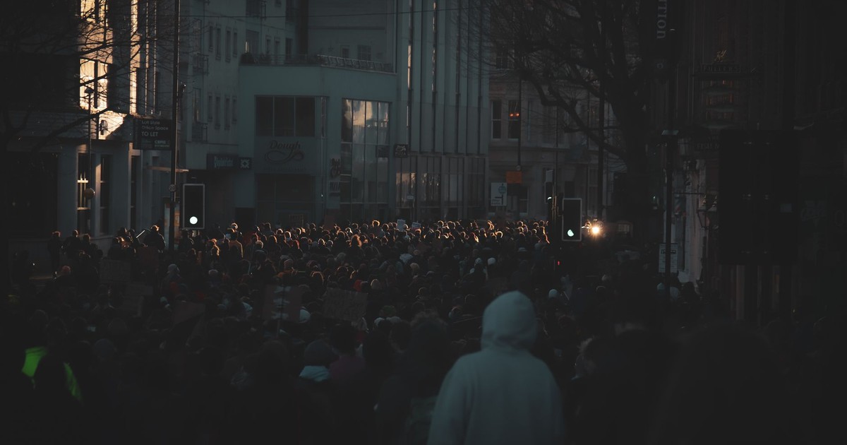 A large crowd gathers for a protest rally on a dimly lit street in Bristol, England.