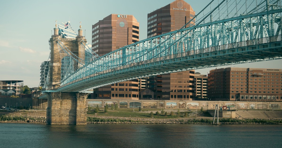 A view of Cincinnati's skyline featuring the iconic Roebling Suspension Bridge over the Ohio River at sunset.