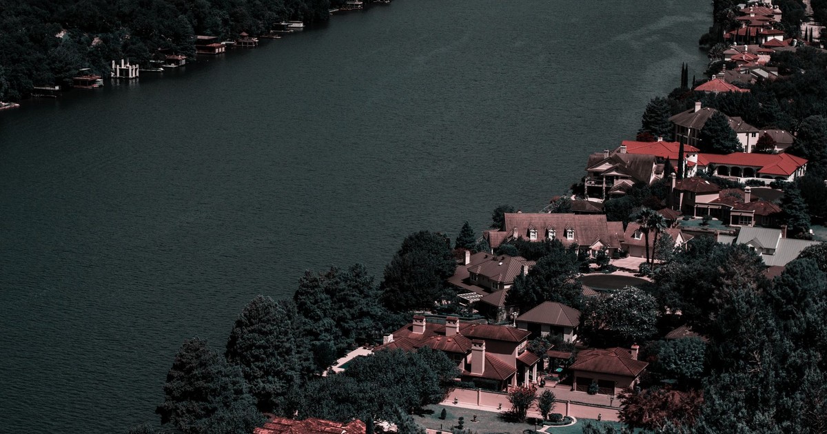 Aerial view of elegant homes along a tranquil river surrounded by lush greenery, showcasing affluence and scenic beauty.