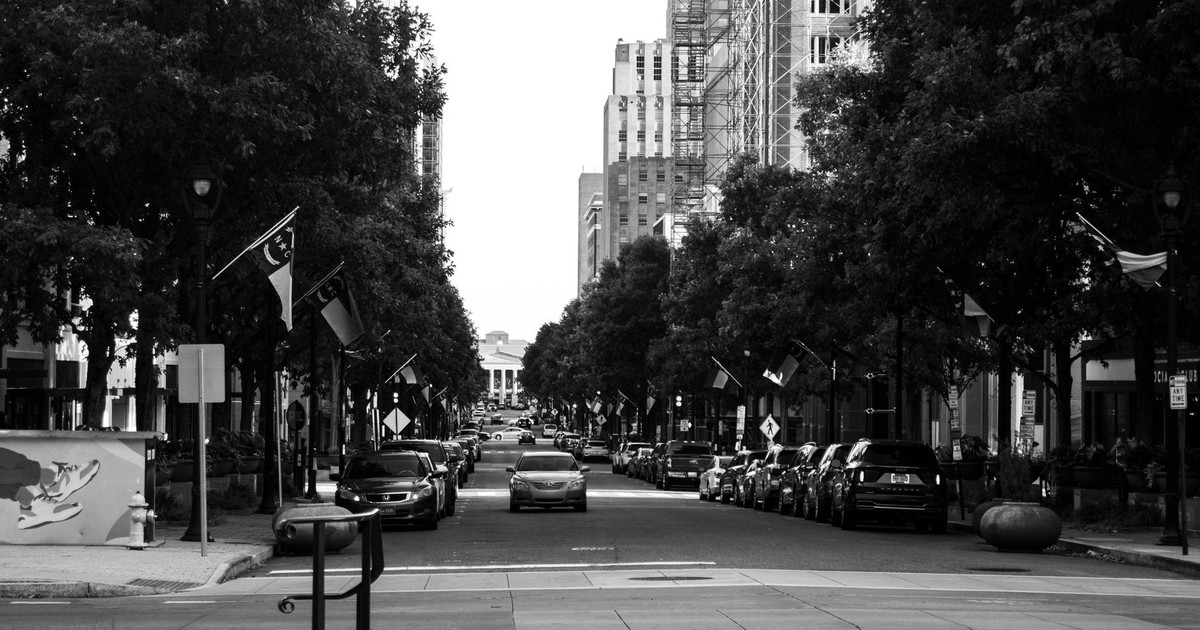 Black and white view of a bustling Raleigh city street with parked cars and flags.