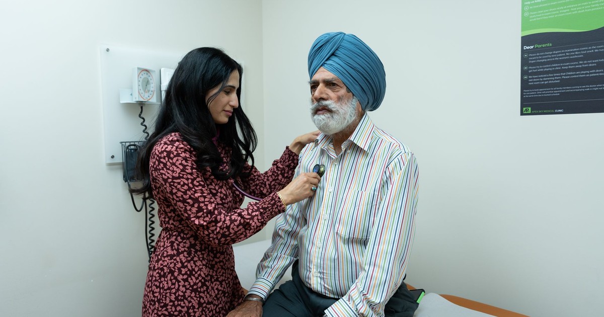 A doctor uses a stethoscope to examine a senior man in an examination room.
