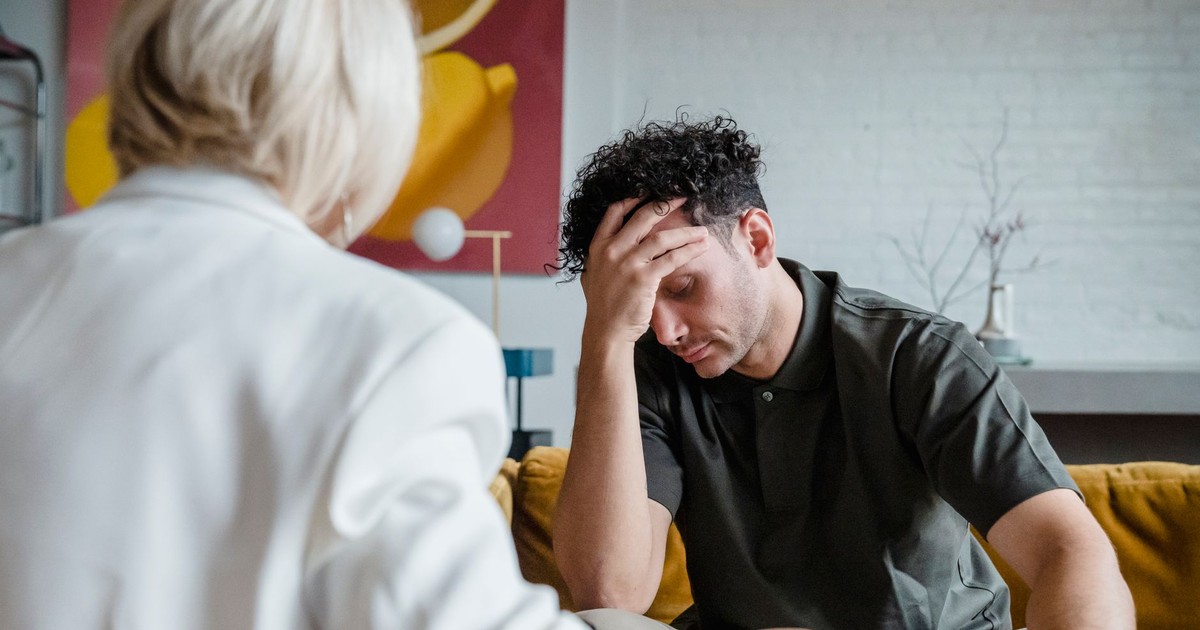 A young man in a therapy session, expressing emotions with hand on forehead.