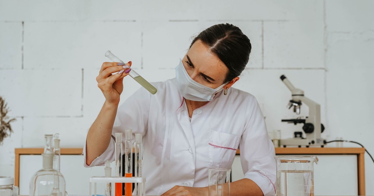 Woman scientist in lab coat examining a test tube with chemical solution, wearing safety mask.
