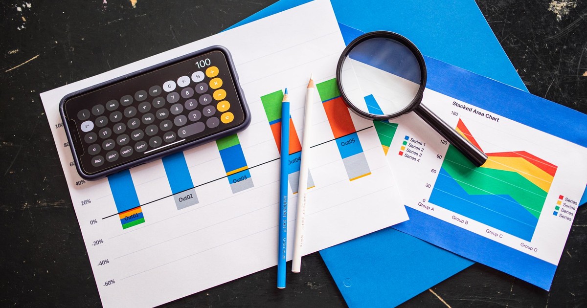Top view of financial charts with a smartphone calculator, magnifying glass, and pencils on a desk.